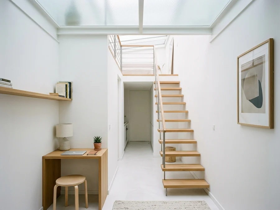 Bright interior of narrowest house with translucent roof, floating wooden stairs, and desk