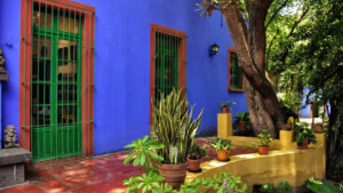 Facade of Frida Kahlo's Blue House in Coyoacán — intense cobalt blue walls with emerald green windows and door, surrounded by lush tropical garden