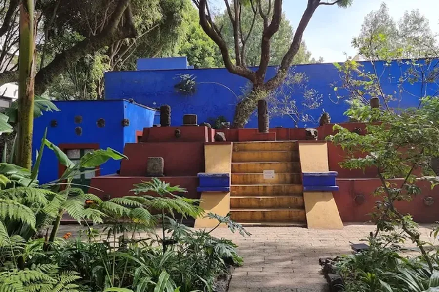 The internal garden of La Casa Azul — terracotta staircase amid dense tropical vegetation, with cobalt blue walls in the background and century-old trees