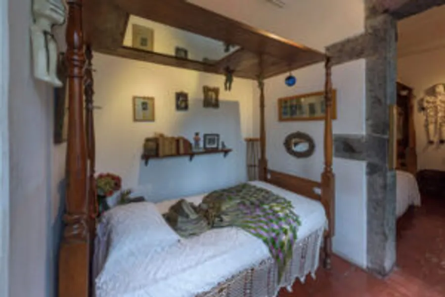 Frida Kahlo's bedroom in La Casa Azul — carved wood four-poster bed with Mexican artisan bedspread, frames and personal objects on the walls, soft natural light