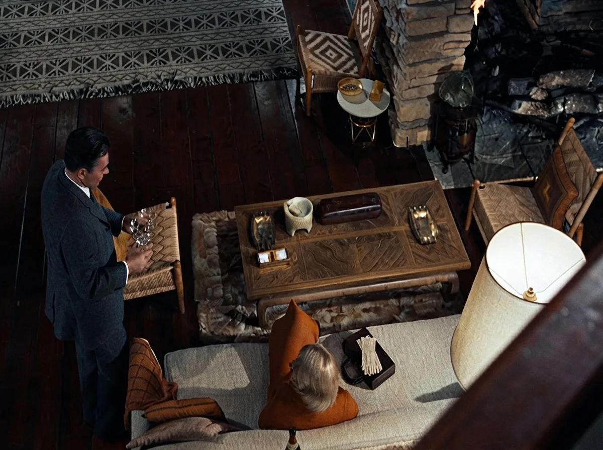 Sala de estar interior da Casa Vandamm com parede de pedra rústica, lareira, escada vazada de madeira e mobília mid-century