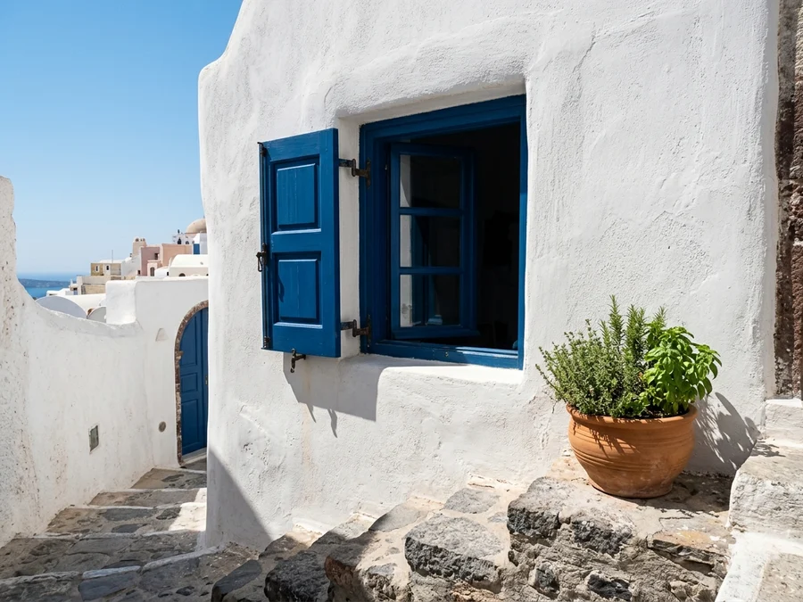 Handmade textured white lime plaster wall with vibrant blue wooden shutter and terracotta herb pot in a Greek village