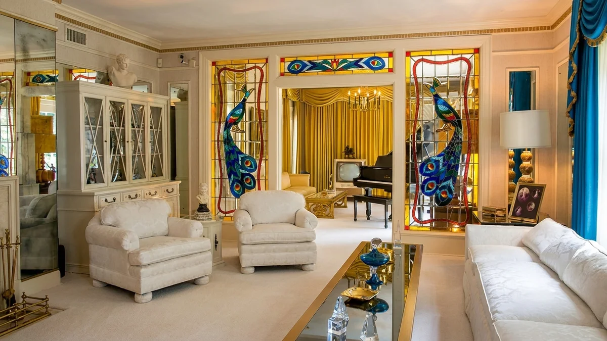 Sala de estar de Graceland com sofás brancos, espelhos e vitrais coloridos de pavões emoldurando a sala de música